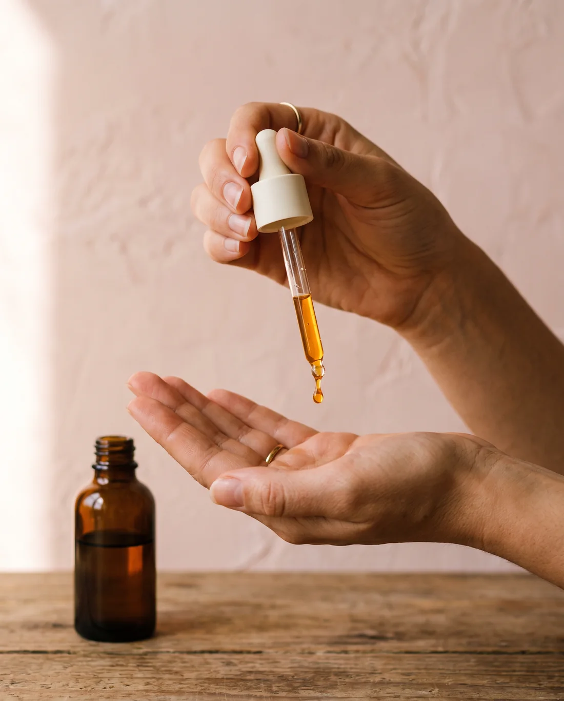 A drop of golden serum falling from the dropper into an open palm